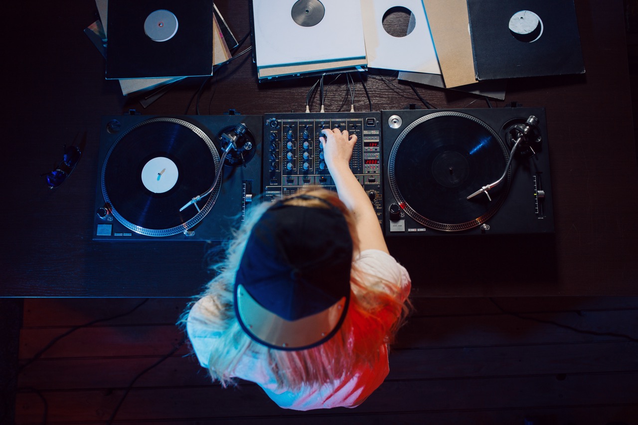 DJ mulher controlando uma mesa de som com discos de vinil, representando o branding pessoal no universo da música e como a imagem de palco contribui para a construção de uma marca autêntica.